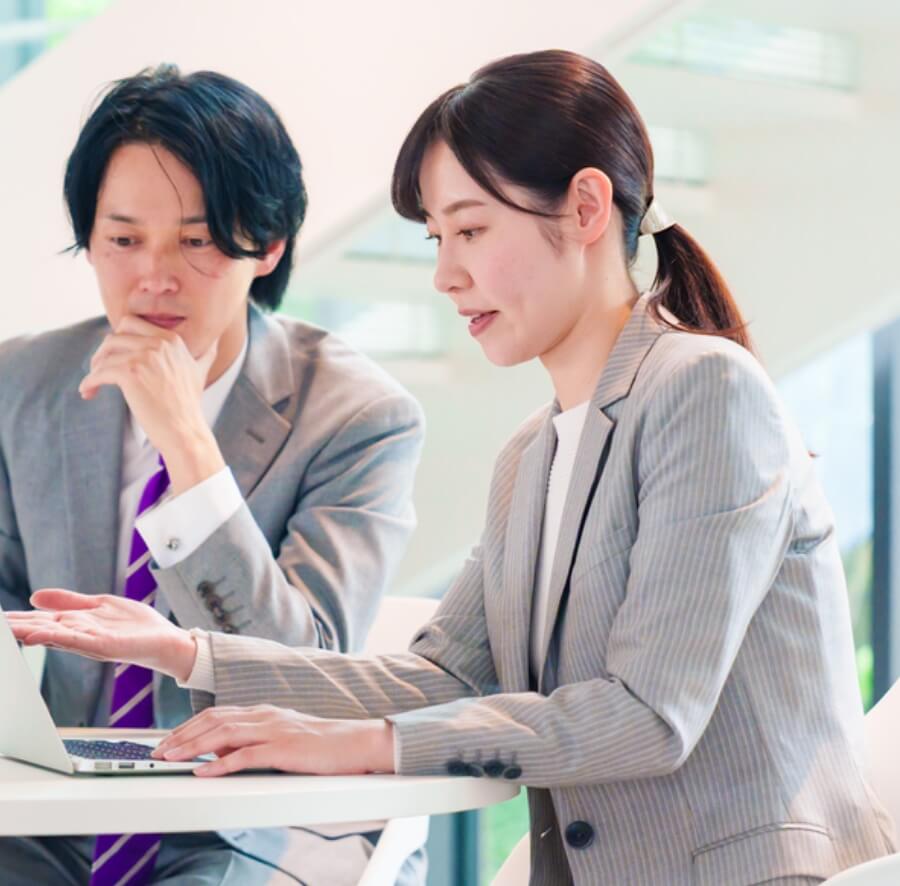 パソコンのある一部を手で示す女性とそれを見ている男性