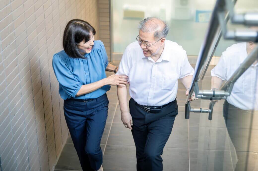 シニアの男性を支えながら一緒に歩く生活支援員の女性