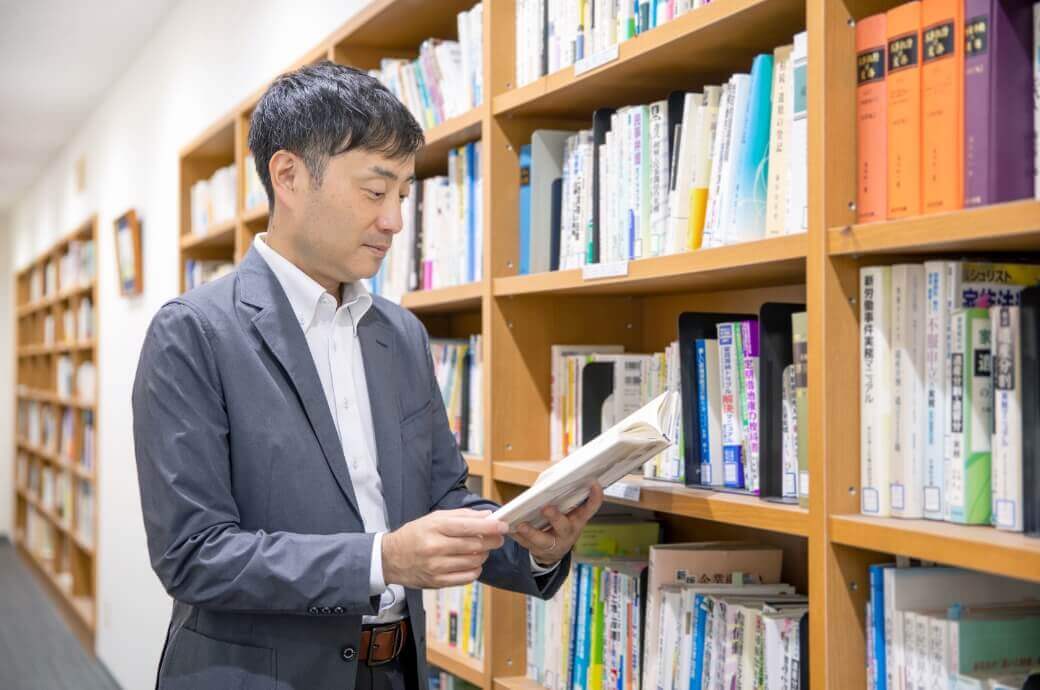 本棚の前で本を読む法務スタッフの男性