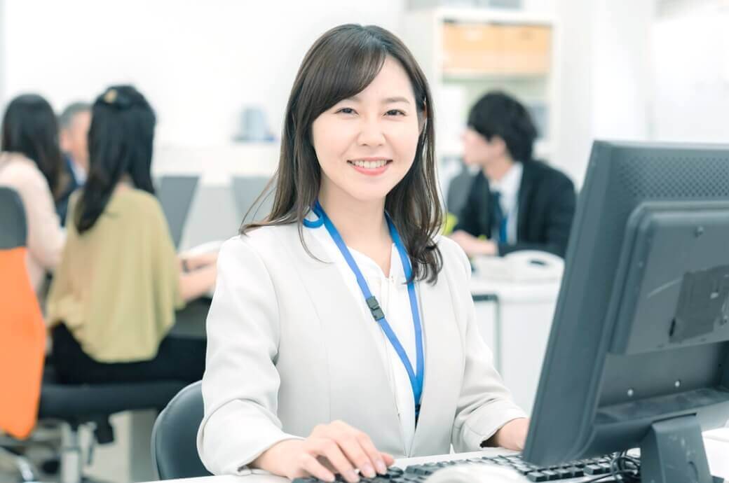 パソコンで作業をしつつ笑っている管理スタッフの女性